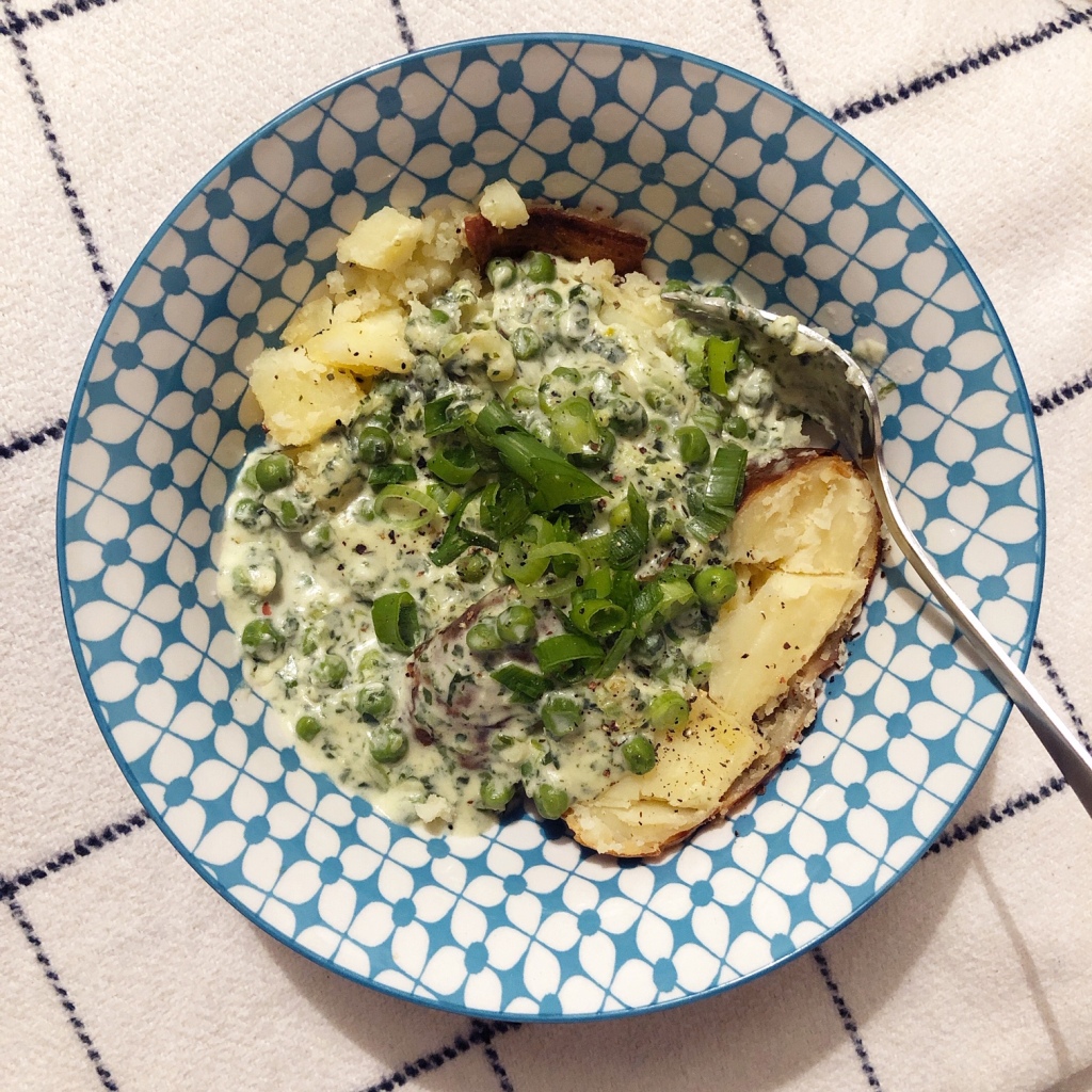 Jacket potato in a bowl with a creamy sauce of peas, spinach and spring onion